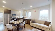 Located at 901 N Market St in the heart of Wilmington, Delaware, this contemporary single-floor residence offers a thoughtfully designed open-concept layout with modern finishes throughout. The combined kitchen, dining, and living area forms the centerpiece of the unit, bathed in natural light through multiple windows that frame sweeping views of the Wilmington cityscape.

The kitchen is outfitted with two-tone cabinetry — crisp white upper cabinets paired with rich dark wood lower cabinets — complemented by white countertops, a subway tile backsplash, and a full suite of stainless steel appliances including a refrigerator, electric range, microwave, and dishwasher. Light wood-style flooring unifies the open living and dining space, contributing to a clean, contemporary aesthetic.

The bedrooms feature neutral carpet flooring and large windows offering striking elevated city views, filling each room with natural light. The bathroom is finished with warm-toned tile work in the tub/shower surround, coordinating floor tile, and a sleek white vanity with an undermount sink. Overall, the residence presents a cohesive, modern design with practical finishes and notable urban vistas throughout.