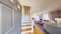 Located at 62 Macarthur Circle East in South Portland, Maine, this cheerful three-floor home offers a well-organized layout across its levels. The main floor features a welcoming living room with warm hardwood floors, natural light from street-facing windows, and a front entry that opens to a cozy seating area accented by nautical-themed artwork. The kitchen is well-equipped with stainless steel appliances, honey-toned wood cabinetry, granite-style countertops, and charming oyster-print wallpaper that adds a coastal character. Tile flooring and ample cabinet storage complete the functional space.

Upstairs, the primary bedroom is generously proportioned, featuring hardwood floors, multiple windows with views of the surrounding greenery, and a relaxed, airy feel. The second bedroom makes a bold design statement with a striking blue checkerboard accent wall, hardwood floors, a closet, and a window providing natural light. The full bathroom is clean and functional, featuring a tub-shower combination with classic finishes. A utility room rounds out the practical amenities. Outside, the property is set on a quiet residential street with mature trees and well-maintained greenery, contributing to its peaceful New England neighborhood charm.