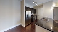 This single-floor residence showcases a cohesive design defined by rich, dark hardwood flooring that extends throughout the living areas and bedrooms, creating a warm and polished aesthetic. Neutral-toned walls complement the overall palette, lending a clean, modern character to the space.

The kitchen is well-appointed with dark espresso cabinetry reaching toward the ceiling for ample storage, dark granite countertops, and a full suite of stainless steel appliances including a French door refrigerator with ice dispenser, electric range, and built-in microwave. A track lighting system illuminates the workspace effectively, while a peninsula with a sink provides additional prep and serving space.

The living area is generously proportioned, featuring a ceiling fan, built-in shelving, and direct access to a private balcony through glass doors flanked by sidelights, offering views of the surrounding neighborhood. Multiple bedrooms feature large, multi-pane windows with roller shades that invite abundant natural light and carry the same outdoor views.

Two full bathrooms are finished with large-format stone-look tile flooring and tub surrounds, soaking tubs, and dark vanity cabinetry with light countertops, offering a functional and well-designed retreat.