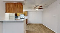 Located at 6131 N 27th Ave in Phoenix, Arizona, this one-bedroom, two-bathroom unit offers a practical and well-organized single-floor layout. The open-concept living and kitchen area serves as the heart of the space, where a peninsula counter visually separates the two zones while maintaining an airy, connected feel. The kitchen features a galley-style design with warm wood cabinetry lining both sides, light countertops, a stainless steel range, a refrigerator, and a built-in ventilation hood — providing ample storage and workspace. A ceiling fan with a light fixture overhead and a painted concrete block accent wall add character to the living area, which is finished with durable wood-look flooring that extends throughout the unit. The bedroom is a comfortable size, featuring vertical blinds on a large sliding glass door that allows natural light to fill the room. The two bathrooms are consistent in style, each featuring warm wood vanity cabinetry, light countertops, large mirrors, and wood-look flooring. One bathroom includes a tub/shower combination. A dedicated closet provides additional storage. The textured ceilings appear throughout the unit, contributing to its classic residential character.