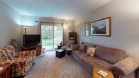 This single-floor residence at 8833 Center Pointe Dr in Baldwinsville, NY offers a thoughtfully arranged layout designed for comfortable, everyday living. The living room serves as the heart of the home, featuring soft carpeting, neutral gray walls, and a large sliding glass door that floods the space with natural light and provides direct views of the lush green outdoors. The open sightlines connect the living area to an entry foyer, which includes practical built-in storage seating and tile flooring that transitions seamlessly into adjacent spaces.

The galley-style kitchen is efficiently organized with warm oak cabinetry lining both walls, light countertops, tile flooring, and a double-basin sink. A louvered pantry door adds additional storage convenience.

The primary bedroom is generously sized, featuring plush carpeting, a large window with outdoor views, and ample space for a sitting area. A second bedroom offers carpet flooring, a sliding double-door closet, and a calm, neutral palette. Both rooms share access to a full bathroom equipped with a wide vanity featuring oak cabinetry, a tub-shower combination with a curtain, safety grab bars, and tile flooring — combining practicality with comfort throughout.