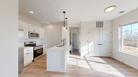 Located at 418 East Genesee Pointe Drive in West Henrietta, NY, this single-floor, 3-bedroom, 2-bathroom home offers a well-designed layout with modern finishes throughout. The open-concept kitchen and living area serves as the heart of the home, featuring white shaker cabinetry, quartz countertops, a peninsula with an undermount sink and matte black faucet, and stainless steel appliances including a refrigerator, range, and microwave. Pendant lighting with glass fixtures illuminates the peninsula, adding a contemporary touch. Light-toned hardwood-style flooring extends through the kitchen and living areas, contributing to a bright, cohesive aesthetic. The spacious living room benefits from natural light streaming through large windows. The primary bedroom includes a closet and hardwood-style flooring, while the additional bedrooms feature plush carpeting, closets, and windows with outdoor views. The bathrooms are finished with white shaker vanities, quartz countertops, matte black hardware, and large framed mirrors. Clean white walls and recessed lighting throughout create a fresh, modern ambiance across the entire home.