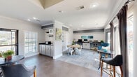This well-appointed business center in Columbia, SC, offers a thoughtfully designed, single-floor layout that balances productivity and comfort. The open-concept space features a mix of flooring, including large-format tile and herringbone-patterned carpet, that visually defines distinct functional zones throughout. Crown molding and recessed lighting add architectural refinement, while gray accent walls and crisp white trim create a clean, contemporary palette.

A dedicated dining area anchors the center of the space, furnished with a round wood table and white metal chairs, ideal for casual meetings or collaborative work sessions. Abstract artwork adorns the walls, lending a creative energy to the environment. Adjacent to the dining area, a built-in coffee bar with gray cabinetry and dark countertops provides a convenient refreshment station.

Workstations line one wall, equipped with computers and ample counter space for individual tasks. A lounge area with tufted blue accent chairs and high-top bar tables offers flexible seating options. Floor-to-ceiling windows and glass doors flood the space with natural light and provide direct views and access to an outdoor patio and pool area. The seamless indoor-outdoor connection enhances the overall sense of openness, making this business center a functional and inviting environment for work and social interaction.