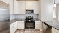 Located at 14329 Liberty Enclave Dr in Charlotte, NC, this well-appointed one-bedroom, one-bathroom residence offers a thoughtfully designed single-floor layout. The kitchen is a standout feature, showcasing crisp white shaker cabinetry, granite countertops with a subway tile backsplash, stainless steel appliances including a side-by-side refrigerator with ice maker, range, microwave, and dishwasher, plus stylish pendant lighting over the peninsula. Light wood-style flooring ties the kitchen together seamlessly. The bedroom is a comfortable retreat, carpeted for warmth and featuring a ceiling fan, a window with natural light and outdoor views, a dedicated walk-in closet with built-in shelving, and direct access to the bathroom. The bathroom mirrors the home's cohesive design with white cabinetry, granite countertops, a large vanity mirror, and wood-look flooring. A dedicated laundry area with a full-size top-load washer and overhead wire shelving adds everyday convenience. Neutral tones and consistent finishes throughout create a clean, modern ambiance well-suited for comfortable living in the Charlotte area.