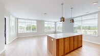 This well-appointed residence offers three bedrooms and two bathrooms across a thoughtfully designed single floor. The open-concept kitchen and living area serves as the heart of the home, featuring warm wood-grain cabinetry, stainless steel appliances, a white quartz-topped island, and stylish pendant lighting. Light hardwood flooring extends throughout the main living areas, while an expansive bank of floor-to-ceiling windows floods the space with natural light and provides views of the surrounding landscaped community.

The living room is generously proportioned, with corner windows that enhance the sense of openness. The kitchen's layout seamlessly connects to the living area, making it ideal for entertaining. A dedicated closet with wire shelving systems provides organized storage.

The bedrooms are carpeted for comfort, each featuring closet access. The primary bedroom includes a dedicated closet. The hallway connects the private areas of the home efficiently, with louvered and panel doors adding architectural detail. Bathrooms are finished with white subway tile and glass-enclosed showers with chrome fixtures. A private balcony with metal railing offers outdoor space overlooking the broader community.
