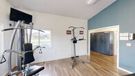 The Mountain View Village Fitness Room and Amazon Hub at 635 Northern Lights Blvd in Box Elder, South Dakota, is a thoughtfully designed community amenity facility spread across a single floor. The space is divided into distinct functional zones, each finished with durable wood-look flooring and accented by a signature teal-blue wall color that lends a modern, cohesive aesthetic throughout.

The fitness center is the heart of the facility, featuring vaulted ceilings with ceiling fans, abundant natural light from multiple windows, and a full complement of equipment. Cardio machines include treadmills, ellipticals, and a stationary bike, while strength training needs are met with a multi-station cable machine, a power tower, a dumbbell rack, and an adjustable bench. Wall-mounted televisions and large mirrors enhance the workout experience. Exercise balls and yoga mats are also available for flexibility and balance training.

Adjacent to the fitness area is a spacious community lounge featuring a full-sized pool table as a central focal point, along with high-top seating, a sofa lounge area, and large windows dressed with sheer curtains that fill the room with natural light. The space is ideal for casual gatherings and recreation.

The facility also includes an Amazon Hub parcel locker station for convenient package retrieval, as well as ADA-accessible restrooms. The overall environment is bright, clean, and welcoming.