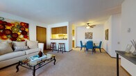 Located at 302 Parkwood Ln in Madison, Wisconsin, this single-floor residence offers a well-organized layout that balances comfort and functionality throughout. The living room is a welcoming space featuring plush wall-to-wall carpeting, large windows with vertical blinds that allow ample natural light, and a ceiling fan overhead. The open-concept design connects the living area seamlessly to the dining space, which accommodates a full dining set, making it ideal for everyday use and entertaining. A pass-through counter with bar-stool seating bridges the living and dining areas to the kitchen, enhancing the sense of openness. The galley-style kitchen is efficiently designed with warm wood cabinetry lining both sides, generous counter space, and white appliances including a range, dishwasher, and refrigerator. An in-unit laundry area is also conveniently located within the kitchen corridor. The residence includes two carpeted bedrooms, each with windows providing natural light and closet space for storage. The full bathroom features a wide vanity with wood cabinetry, a white countertop, a large mirror, tile flooring, and baseboard heating. The overall layout is practical and comfortable, making this Madison residence a well-appointed home.
