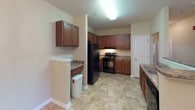 This single-floor residence offers three bedrooms and two full bathrooms, designed with a practical and cohesive layout. The kitchen is well-equipped with rich medium-toned wood cabinetry, granite-look countertops, black appliances including a range and refrigerator, and tile flooring in a natural stone pattern. A breakfast bar provides a convenient transition into the adjoining dining area, which features tile flooring and an elegant chandelier overhead. The living area flows naturally from the dining space and is finished with neutral carpet, creating a comfortable and unified feel.

The bedrooms are carpeted and painted in warm neutral tones. The primary bedroom benefits from multiple windows that bring in natural light and includes a ceiling fan. A walk-in closet with wire shelving and hanging rods offers organized storage. The additional bedrooms are similarly finished, each with windows and neutral carpet.

The two bathrooms mirror each other in style, featuring the same stone-patterned tile flooring and wood vanity cabinetry with light countertops. One bathroom includes a shower-tub combination. Throughout the home, consistent finishes and a neutral color palette create a clean, cohesive atmosphere.
