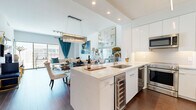 Located in Dallas's vibrant Uptown neighborhood, this thoughtfully designed one-bedroom, one-bathroom residence offers a seamless blend of modern aesthetics and functional living. Rich hardwood flooring flows throughout, anchoring the bright, open-concept layout that connects the kitchen, dining, and living areas into a cohesive, airy space.

The kitchen is a standout feature, showcasing high-gloss white cabinetry, subway tile backsplash, stainless steel appliances including a built-in range and French door refrigerator, and a large central island with a quartz countertop, undermount sink, and integrated wine refrigerator — ideal for both everyday cooking and entertaining.

The combined dining and living area is generously proportioned, bathed in natural light from floor-to-ceiling windows and offering direct access to a balcony with sweeping Dallas skyline views. The bedroom continues the refined aesthetic with a textured feature wall, a gold chandelier, and expansive glass sliding doors that frame impressive city vistas.

The bathroom features a soaking tub, modern vanity, and direct access to a spacious walk-in closet with adjustable shelving systems. Additional conveniences include an in-unit laundry area, a hallway with entry closet, and recessed lighting throughout, rounding out this polished urban residence.