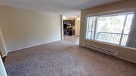Located at 4700 176th St SW in Lynwood, Washington, this single-floor residence offers a well-organized and functional layout throughout. The open living and dining area is finished with plush wall-to-wall carpeting and features large windows alongside a sliding glass door that opens to a private balcony, inviting generous natural light and outdoor views of surrounding greenery. Baseboard heating units are present throughout the living spaces, ensuring consistent warmth. A ceiling fan adds additional comfort to the main living area.

The galley-style kitchen is efficiently designed with rich, dark espresso cabinetry, stone-toned countertops, and wood-look vinyl flooring. It is equipped with a full suite of black appliances including a refrigerator, stove, and dishwasher, along with a stainless steel sink. A window at the end of the kitchen corridor further enhances the sense of light and openness.

The bedrooms are generously sized, each carpeted and featuring dedicated closet space, including a walk-in closet in the primary bedroom. Neutral warm-toned walls and textured ceilings are consistent throughout the home, creating a cohesive and understated aesthetic. The overall layout is practical and well-suited for comfortable everyday living.