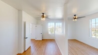 This single-floor space combines clean, modern finishes with classic architectural details to create a bright and functional living environment. Throughout the main living and bedroom areas, light-toned hardwood flooring provides a warm foundation, complemented by crisp white walls and white baseboards that enhance the sense of openness. Ceiling fans with brushed gold hardware are installed in multiple rooms, adding both functionality and a refined aesthetic touch.

Large, gridded double-hung windows are a defining feature of the space, allowing generous natural light to pour in while framing elevated views of the surrounding urban landscape, including tree-lined streets and distant hills. The windows contribute significantly to the airy, well-lit atmosphere present throughout.

The kitchen stands out with bold navy blue cabinetry, stainless steel appliances, white subway tile backsplash, and butcher block open shelving supported by decorative brackets. A matte black faucet and sink complete the cohesive, design-forward look.

The bathroom continues the design theme with floor-to-ceiling white subway tile surrounding a tub/shower combination, accented by matte black fixtures and hardware, including a towel ring and faucet set. A window above the tub introduces natural light into the space. The overall ambiance is clean, contemporary, and thoughtfully finished.