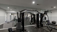 Located at 1108 Saint Andrews Dr in Wilmington, NC, this single-floor fitness center offers a comprehensive workout environment thoughtfully organized across several functional zones. The main exercise area is lined with large floor-to-ceiling mirrors that amplify the sense of space and allow users to monitor their form throughout their workouts. Durable rubber flooring covers the entire gym floor, providing both safety and comfort underfoot.

The strength training zone is well-appointed with a multi-station cable machine, a full dumbbell rack with a wide range of weights, and multiple adjustable benches suited for a variety of exercises. The cardio section features treadmills, a stationary bike, a Landice elliptical, and additional cycle machines, all positioned to take advantage of natural light streaming through large windows. A wall-mounted television is installed in the cardio area for entertainment during workouts.

Recessed lighting throughout ensures bright, even illumination across all areas. White beadboard wainscoting adds a clean, finished aesthetic to the walls, complemented by a neutral white-and-gray color palette. Storage shelving is available for personal belongings. The facility also includes a dedicated laundry room equipped with multiple commercial-grade washers and dryers, offering added convenience for residents.