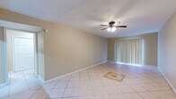 This single-floor space offers a functional and cohesive layout connected by light ceramic tile flooring throughout. The spacious living area is a standout feature, highlighted by a decorative tile inlay at its center, a ceiling fan with integrated lighting, and a large sliding glass door dressed with vertical blinds that floods the room with natural light. The open feel of this main area makes it an inviting and versatile space.

The kitchen is well-designed with a bold, contemporary aesthetic. Dark espresso cabinetry pairs with granite-style countertops and a textured stone tile backsplash, creating a striking contrast. The kitchen is equipped with a black refrigerator, a range, and an under-cabinet range hood, along with ample storage and counter space, including an extended breakfast bar-style counter.

The bedroom continues the consistent tile flooring and features its own ceiling fan with lighting and a window fitted with horizontal blinds, allowing for natural light and ventilation. The bathroom is practical and clean, offering a single vanity with dark cabinetry and a granite-style countertop, a soaking tub, and a tiled surround. A hallway connects the bathroom to the bedroom, maintaining an efficient and organized flow throughout the space.