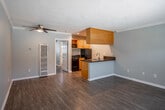 Located at 907 S Harbor Blvd in Santa Ana, California, this single-floor unit offers a practical and well-appointed layout designed for comfortable everyday living. The open-concept living area flows seamlessly into the kitchen, creating a connected and functional space. Hardwood-style laminate flooring runs throughout, providing a cohesive and easy-to-maintain surface, while textured ceilings and crown molding add a classic finishing touch.

The kitchen is efficiently designed in a galley style, featuring warm honey-toned wood cabinetry, dark granite-style countertops, a stainless steel sink, and black appliances including a gas range and refrigerator. A peninsula with an overhang connects the kitchen to the living space, offering casual seating or serving opportunities. Recessed lighting illuminates the kitchen area.

The living room benefits from a ceiling fan with light fixture, neutral gray walls, and a large front-facing window that allows ample natural light to filter in, with views of the surrounding outdoor area. A wall-mounted AC unit provides additional climate control.

The bedroom is a comfortable, well-proportioned room with its own ceiling fan, a window for natural light, and the same hardwood-style flooring. The bathroom includes a full tub and shower combination, a toilet, and a small window for ventilation. Throughout the unit, clean white baseboards and neutral tones create a bright, welcoming ambiance.