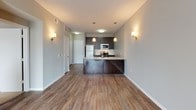 This single-floor unit offers a well-designed, open-concept layout that seamlessly connects the kitchen and living areas. The kitchen is a standout feature, equipped with dark espresso cabinetry, granite-style countertops, and a full suite of stainless steel appliances, including a refrigerator, electric range, and over-the-range microwave. A subway tile backsplash adds a clean, contemporary touch, while a peninsula with pendant lighting above provides additional prep space and casual seating. Warm-toned hardwood-style flooring runs throughout the unit, lending a cohesive and inviting aesthetic. Wall sconces in the living area contribute to a comfortable, well-lit ambiance. The living space is bright and open, with a sliding glass door that leads to a private balcony, allowing natural light to fill the room and offering views of the surrounding exterior. The bathroom features a combination soaking tub and shower with tiled surround accented by a decorative mosaic column, complemented by a dark-finished vanity with a light countertop. The overall design balances modern finishes with functional, everyday living.