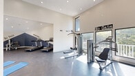 This fitness center in Memphis, TN offers a generously sized, single-floor exercise space designed to support a well-rounded workout routine. The facility features soaring vaulted ceilings that lend an open, airy feel throughout, complemented by recessed lighting and large windows on multiple walls that flood the interior with natural light and provide views of the surrounding greenery.

The exercise room is divided into functional zones. A dedicated cardio area hosts multiple treadmills positioned along a boldly accented navy blue accent wall, complete with motivational phrases such as "No Excuses" and "No Pain." A separate strength-training zone includes a multi-function cable machine, a weight bench, a leg press machine, and additional resistance equipment. Cycling enthusiasts will find stationary bikes available as well. A stretch and yoga area provides blue exercise mats laid out on the durable dark rubberized flooring, offering ample room for floor exercises and cool-downs.

The interior design balances clean white walls with striking navy blue geometric accents, creating an energizing yet modern atmosphere. The dark, low-maintenance flooring throughout provides a practical and polished finish. With wide open floor space, varied equipment options, and a bright, motivating environment, this fitness center is well-suited for a diverse range of workout preferences and fitness goals.