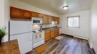 Located at 1324 18th Ave S in Fargo, North Dakota, this single-floor unit offers a straightforward, functional layout with a clean and well-maintained interior. The entryway opens onto durable wood-style plank flooring that extends through the main living areas, providing a cohesive and easy-to-maintain surface. The spacious living room is defined by a large picture window dressed with vertical blinds, allowing abundant natural light to fill the room, and is equipped with baseboard heating along the exterior wall.

The kitchen features warm honey-toned wood cabinetry with ample upper and lower storage, granite-style countertops, and white appliances including a refrigerator, electric range, over-the-range microwave, and dishwasher. A window above the sink area brings in additional daylight. The layout connects efficiently to the rest of the unit via a hallway with wood-style flooring.

The bedrooms are carpeted for comfort and each include multiple windows with vertical blinds, baseboard heating, and flush-mount ceiling lighting. The bathroom includes white tile wainscoting, a shower/tub combination with a curtain, a wall-mounted mirror, and a vanity with a white basin. Textured ceilings are present throughout, contributing to the unit's classic character.