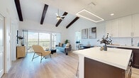Located at 1002 N Fourth St in Flagstaff, AZ, this well-appointed 3-bedroom, 2-bathroom single-story home offers a thoughtfully designed layout with modern finishes throughout. The open-concept living room is a standout, featuring soaring vaulted ceilings accented by dark wood beams, light hardwood flooring, and large sliding glass doors that open to a private balcony overlooking a lush Ponderosa pine forest. The kitchen is a chef's delight, boasting a two-toned design with crisp white upper cabinets and rich dark lower cabinetry, a generous center island with bar seating, stainless steel appliances, and a sleek suspended linear pendant light. A dedicated hallway connects to both bathrooms and all three bedrooms. The spacious primary bedroom features vaulted ceilings, a ceiling fan, large windows framing treetop views, and access to a dedicated walk-in closet. The primary bathroom offers a clean, contemporary aesthetic with a wide white vanity, backlit mirror, tile flooring, and a glass-enclosed shower. A secondary bedroom, finished in a similarly warm and neutral palette with hardwood floors, is served by a well-appointed second bathroom with white cabinetry and tile floors conveniently positioned near the kitchen.