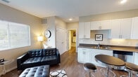 Located at 14820 Piper Ln in Grand Haven, Michigan, this single-floor unit offers a thoughtfully designed layout that blends modern aesthetics with everyday functionality. The open-concept living and kitchen area serves as the heart of the space, where warm hardwood-style flooring flows seamlessly throughout. The living room provides generous space for comfortable seating, with a large window that invites natural light and offers views of the surrounding neighborhood. The kitchen is well-equipped with crisp white shaker-style cabinetry, dark countertops, and a full suite of stainless steel appliances including a refrigerator, electric range, and over-the-range microwave. A compact breakfast bar with stylish round stools adds a casual dining option that complements the kitchen's modern character. The bedroom features soft carpeting, a sliding-door closet with built-in shelving, and a window that allows for natural light. The bathroom is finished with a single-sink vanity, clean white cabinetry, and hardwood-style flooring that ties back to the rest of the unit. Throughout, neutral wall tones and recessed lighting create a bright, welcoming ambiance suited for comfortable everyday living.