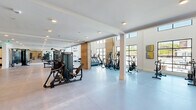 Located at 1801 Riverside Parkway in Douglasville, Georgia, this expansive fitness facility delivers a comprehensive and professionally designed workout environment across a single floor. The space is divided into three distinct exercise rooms and a connecting hallway, each area thoughtfully outfitted to support a wide range of training styles.

The main exercise area is expansive and open, featuring polished concrete floors, recessed lighting, and an extensive array of strength and resistance machines. Warm wood-panel accent walls add a modern, inviting contrast to the crisp white walls, which are adorned with motivational typography. Floor-to-ceiling windows in select areas flood the space with natural light and offer outdoor views, enhancing the overall ambiance.

A dedicated cardio room features soaring ceilings with oversized black-framed windows, housing air bikes, rowing machines, and cycling equipment. An adjacent room provides space for functional training with equipment such as cable machines, adjustable benches, and plyo boxes.

The hallway is a standout feature, lined with vibrant artificial turf flooring—ideal for sled pushes and agility drills—flanked by two-tone painted walls in white and steel blue. Together, these spaces create a dynamic, well-rounded fitness facility suited for a broad spectrum of athletic training needs.