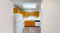 Located at 11500 Kings Crest Ct in Fredericksburg, VA, this one-bedroom, one-bathroom residence offers a practical and well-organized single-floor layout. The kitchen and living room share an open, connected space, creating a functional flow for everyday living. The kitchen is outfitted with warm honey-toned wood cabinetry — both upper and lower — along with white appliances including a refrigerator, range, and dishwasher. A sink with under-cabinet storage anchors the workspace, and wood-style luxury vinyl flooring runs throughout the kitchen area, adding a clean, modern touch. A ceiling fan overhead in the living area enhances comfort, and a sliding glass door provides natural light and outdoor views. The bedroom is a comfortable, well-proportioned space with soft carpeting, a window that brings in natural light, and access to two closets for ample storage. The bathroom features a tiled shower and tub combination with accessibility grab bars, providing both safety and functionality. Neutral wall tones and textured ceilings are consistent throughout, lending the unit a cohesive and move-in-ready aesthetic. This unit is well-suited for those seeking a straightforward, low-maintenance living space in Fredericksburg.