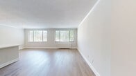This thoughtfully designed 1-bedroom, 1-bathroom apartment offers 670 square feet of efficiently utilized single-floor living space. Light oak hardwood flooring flows consistently throughout the entire unit, creating a warm and cohesive aesthetic. The open living area is bright and airy, featuring large windows with horizontal blinds that frame lush outdoor greenery and allow generous natural light to fill the space. Crown molding and textured ceilings add a classic architectural touch to the main living areas. The galley-style kitchen is a standout feature, offering two-tone cabinetry with warm wood lower cabinets and crisp white uppers, white quartz countertops, a subway tile backsplash, and stainless steel appliances including a gas range, microwave, and refrigerator. The primary bedroom spans 180 square feet, is fitted with a built-in closet with paneled bifold doors, recessed lighting, and a window overlooking the outdoors. The bathroom features full tiled walls in warm beige tones, a soaking tub with shower, a wood-toned vanity with white countertop, and coordinating hardwood flooring. A dedicated entryway with a decorative column detail completes this clean, modern apartment.