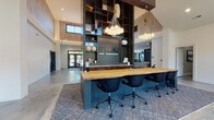 Located at 168 Headwater Circle in Mooresville, North Carolina, this single-story leasing office for Elevate Lake Norman presents a thoughtfully designed, contemporary space that balances professional functionality with refined aesthetics. The interior is immediately distinguished by its soaring vaulted ceilings, which lend an expansive, airy quality throughout.

At the heart of the space is a striking live-edge wood communal workstation, finished in natural tones and paired with sleek black ergonomic chairs. This central feature is anchored by a bold, dark-framed open shelving unit that rises dramatically toward the ceiling, displaying curated décor and bearing the Elevate Lake Norman branding. Overhead, sculptural globe pendant chandeliers in warm brass provide both ambient and focused illumination, complementing the polished concrete flooring below.

The layout transitions smoothly from the open main area into a more defined workspace, where warm wood cabinetry topped with white stone countertops lines one wall, offering additional functionality. Large windows along the perimeter invite generous natural light, offering views of the surrounding greenery. Abstract wall art and thoughtfully placed accent furnishings add a curated, upscale character to the overall ambiance, making this office both welcoming and professional.