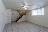 Located on Topping Avenue in Kansas City, Missouri, this two-story property offers a practical and straightforward layout distributed across two distinct levels. The lower floor serves as the main living area, featuring generously sized open rooms finished with light ceramic tile flooring. Ceiling fans are present throughout, providing airflow and understated overhead lighting. A textured popcorn ceiling and neutral-toned walls characterize this level, while a window fitted with blinds allows natural light to enter the main living space. A staircase with a dark wood finish and metal railing connects the lower level to the upper floor. The kitchen on this level includes warm-toned wood cabinetry arranged in an L-shaped configuration, a double-basin sink, dark granite-style countertops, and an overhead ventilation hood. A compact half bathroom on the lower level features tile flooring, a single-sink vanity with a white cabinet, and a wall-mounted mirror. The upper floor transitions to hardwood flooring in a rich honey tone, carrying through multiple rooms that are bright and well-proportioned, each equipped with ceiling fans. A full bathroom on the upper level includes a tiled shower-tub combination and tile flooring.