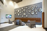 Located at 4558 Roswell Rd NE in Sandy Springs, Georgia, this single-floor amenity space presents a sophisticated, modern design characterized by a cohesive neutral palette, dark wood accents, and carefully curated furnishings. The open layout flows seamlessly between distinct functional zones, each finished with large-format tile flooring that grounds the contemporary aesthetic.

The kitchen area serves as a central gathering point, featuring dark espresso cabinetry, a bold geometric mosaic tile backsplash, and stainless steel appliances. A generous white quartz island is surrounded by upholstered bar seating and illuminated overhead by a series of elegant capiz shell pendant lights, creating an inviting, well-lit environment.

The lounge area commands attention with soaring ceilings and a dramatic feature wall — a dark paneled backdrop adorned with an arrangement of convex mirrors. Plush mid-century-inspired lounge chairs and built-in banquette seating provide comfortable gathering space, complemented by a wall-mounted display screen and a sculptural sputnik chandelier.

A striking dark-stained staircase with refined iron railings connects levels, while an adjacent dining table offers additional workspace or meeting capacity. Steel-framed glass doors provide a transparent connection to the fitness center beyond, bringing in natural light and visual openness throughout.