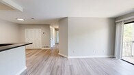 This 3-bedroom, 2-bathroom residence offers a clean, modern aesthetic defined by light gray walls, white trim, and light wood-look luxury vinyl plank flooring throughout the main living areas. The open-concept living room connects seamlessly to the kitchen via a peninsula counter with a dark laminate countertop and built-in sink, ideal for casual dining or meal prep. The kitchen is equipped with white cabinetry, black appliances including a gas range, microwave, and refrigerator, and tile flooring. The living room features a sliding glass door that opens to a private balcony with outdoor views of surrounding greenery, filling the space with natural light. Two of the bedrooms feature plush wall-to-wall carpeting and windows with garden views, while one bedroom offers sliding door access to an additional outdoor area. The generously sized primary bedroom includes a dedicated walk-in closet with wire shelving. The two bathrooms are finished in a crisp white palette, with one featuring a full tub-shower combination with sliding glass doors, a single-sink vanity, and wood-look flooring. Bifolding closet doors and recessed lighting add functional detail throughout. The overall ambiance is bright, clean, and move-in ready.