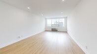 This 1-bedroom, 2-bathroom residence offers a clean, modern aesthetic defined by light hardwood flooring, crisp white walls, and recessed lighting throughout. The open living room is generously proportioned, bathed in natural light from large windows that frame striking urban skyline views, creating an airy and inviting atmosphere. A wall-mounted climate control unit ensures year-round comfort.

The kitchen is well-equipped and stylish, featuring light wood cabinetry extending to the ceiling for ample storage, a marble-veined quartz backsplash and countertops, stainless steel appliances including a French door refrigerator, range, and dishwasher, all set atop the same warm hardwood flooring that flows throughout the residence.

The primary bedroom is a comfortable, well-sized retreat with recessed lighting and large windows offering continued city views. A dedicated closet provides organized storage.

Both bathrooms are finished to a high standard, featuring light wood vanities topped with marble-veined quartz countertops, neutral tile flooring, and matte black hardware accents. One bathroom includes a glass-enclosed walk-in shower with marble-style tile surround, while both maintain a clean, contemporary design. The overall ambiance of the residence is bright, modern, and move-in ready.