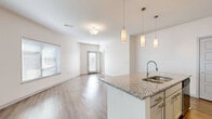 Located at 601 Avenida Cesar E Chavez in Kansas City, MO, this 1-bedroom, 1-bathroom unit offers a well-designed, single-floor layout with modern finishes throughout. The open-concept living area seamlessly connects the kitchen, dining, and living spaces, all finished with warm wood-look flooring and bathed in natural light from large windows fitted with blinds. A private balcony extends the living space outdoors.

The kitchen is a standout feature, centered around a large island with granite countertops, an undermount double sink, and elegant pendant lighting. White cabinetry, a subway tile backsplash, stainless steel appliances — including a refrigerator, range, and microwave — and track lighting complete the space.

The bedroom is carpeted for comfort and receives abundant natural light through wide windows. A ceiling fan adds convenience, and the room connects directly to the bathroom and a spacious walk-in closet with built-in wire shelving. A second closet provides additional storage.

The bathroom features granite countertops, a single undermount sink, gray cabinetry, and wood-look flooring. Dedicated laundry and utility rooms round out the functional layout of this thoughtfully designed Kansas City residence.