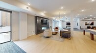 Located at 375 W Whitney Ave in Salt Lake City, Utah, this generously sized amenity center offers a well-rounded collection of social and recreational spaces spread across a single level. The interior is characterized by a clean, contemporary design with white walls, recessed lighting, and a seamless blend of light hardwood flooring and plush patterned carpet throughout.

The open-plan kitchen and entertaining area anchors one end of the space, featuring warm wood cabinetry, a subway tile backsplash, open shelving, stainless steel appliances, and a large central island with bar seating — ideal for community gatherings and events. Pendant lighting adds a modern touch overhead.

Adjacent to the kitchen, a spacious game and lounge area includes a full shuffleboard table and flows into a carpeted zone with comfortable seating arrangements, including a sectional sofa, accent chairs, and a wall-mounted television. A dedicated billiards room provides a more intimate setting with a full-size pool table, recessed lighting, and locally inspired wall art.

A separate lounge nook offers a round table with seating and additional TV access, perfect for casual meetings or small group gatherings. The space opens to a private courtyard surrounded by a modern multi-story building facade featuring mixed materials including wood paneling, metal cladding, and brick, with outdoor seating and landscaped planters.