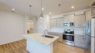 Located at 9000 Palm Passage Loop in Summerville, SC, this well-appointed 2-bedroom, 1-bathroom single-story home offers a thoughtfully designed layout with modern finishes throughout. The open-concept kitchen and living area serves as the heart of the home, highlighted by a large central island topped with granite countertops, an undermount sink, and stylish pendant lighting. Gray shaker-style cabinetry, a herringbone tile backsplash, and a full suite of stainless steel appliances — including a refrigerator, range, and over-the-range microwave — complete the kitchen. Light wood-look flooring flows through the main living areas, adding warmth and continuity. The living room features French doors with transom windows, a ceiling fan with integrated lighting, and abundant natural light. Both bedrooms are carpeted and include ceiling fans; the primary bedroom offers a comfortable, well-proportioned retreat. The bathroom is fitted with a soaking tub and shower combination with white tile surround. A dedicated laundry room accommodates a full-size washer and dryer with wire shelving above. Clean white walls and recessed lighting throughout give the home a bright, contemporary feel.