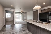 Located at 1360 NE Primrose Ln in Grimes, Iowa, this 1-bedroom, 1-bathroom residence offers a thoughtfully designed single-floor layout that maximizes functionality and comfort. The open-concept kitchen and living area serves as the heart of the home, where wood-look luxury vinyl flooring flows seamlessly underfoot. The kitchen features a peninsula with a double-basin sink and pendant lighting overhead, dark-toned cabinetry, a black refrigerator, and a black range with over-the-range microwave — all complementing the neutral countertops. The living area extends naturally from the kitchen, finished with plush carpeting and a ceiling fan, and opens directly onto a private balcony through sliding glass doors, bringing in natural light and outdoor access. A dedicated pantry provides additional storage. The bedroom is a comfortable, carpeted retreat with a window offering natural light, and is serviced by a well-sized closet. The bathroom includes a dark-cabineted vanity with a sink, mirror, and wood-look flooring. A dedicated laundry room houses a full-size washer and dryer with built-in wire shelving above. The textured ceilings and neutral color palette throughout create a clean, cohesive aesthetic.