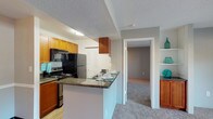 This single-floor residence offers a thoughtfully designed layout that balances functionality and comfort throughout. The kitchen is a standout feature, equipped with warm wood cabinetry, dark granite countertops, black appliances including a refrigerator, electric range, and microwave, as well as a stainless steel sink. Wood-look flooring runs through the kitchen, which also includes a breakfast bar that opens toward the living and dining area. The living room is generously proportioned, finished with soft carpeting and neutral gray walls, and features a sliding glass door that opens to an outdoor patio, allowing natural light to fill the space. An adjoining dining area transitions seamlessly between the kitchen and living room. The bedrooms are carpeted and feature neutral tones with windows that bring in natural light. Each bedroom is well-served by closet storage, with one room showcasing a double-door closet with built-in shelving for ample organization. The bathroom is finished with granite countertops, a wood vanity, an undermount sink, a full tub and shower combination with white tile surround, and tile flooring. Textured ceilings are consistent throughout the home, contributing to its classic residential character.