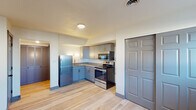 This single-floor space offers a clean, contemporary layout designed for comfortable everyday living. Light-toned hardwood flooring runs throughout, providing a warm and cohesive foundation that unifies each area of the unit. Dark-painted baseboards and interior doors create a striking contrast against the crisp white walls, adding a modern design touch.

The main living area is generously proportioned, featuring multiple windows that invite abundant natural light and offer views of the surrounding neighborhood. A set of dark double doors provides additional storage or closet space within the room.

The kitchen is efficiently designed and well-appointed, showcasing two-tone grey shaker-style cabinetry with brushed gold hardware. Granite countertops provide a durable and attractive work surface, complemented by a stainless steel undermount sink with a matching gold-finish faucet. Stainless steel appliances — including a refrigerator, electric range, and over-the-range microwave — complete the kitchen's functional and stylish aesthetic. The open sightlines between the kitchen and living area enhance the sense of space throughout.

Additional rooms include a secondary open area that can serve as a bedroom or flex space, accessible via the same charming dark-painted doors consistent with the rest of the unit's design language. Overall, the space presents a well-finished, move-in ready interior with thoughtful material choices throughout.