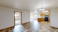 Located at 39th Ave SE in Minot, North Dakota, this single-floor, 3-bedroom, 2-bathroom home offers a well-organized and functional layout across a comfortably sized footprint. The open-concept kitchen and dining area serves as the heart of the home, featuring warm honey-toned wood cabinetry, generous counter space, a central peninsula, stainless steel appliances including a refrigerator, dishwasher, and over-the-range microwave, complemented by durable tile-style flooring. A pendant chandelier adds a finishing touch above the dining area. The living room is spacious and bright, with multiple windows framing outdoor views and direct access to the outdoors through a glass door, filling the room with natural light. Plush carpeting and baseboard heating run throughout the bedrooms, which are well-proportioned and include ample closet storage across four closets. The bathrooms are clean and functional, featuring a full tub-shower combination with white tile surround. A dedicated in-unit laundry room houses a full-size washer and dryer. Neutral wall tones, warm wood trim, and consistent finishes throughout give the home a cohesive and inviting character well-suited to comfortable everyday living.