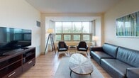 Located at 8 Kimball Ct in Burlington, Massachusetts, this single-floor residence offers a thoughtfully designed layout that balances comfort and functionality. The open-concept living area is anchored by warm hardwood flooring and a generous bank of windows that flood the space with natural light and frame views of the surrounding greenery. The living room accommodates multiple seating arrangements, with ample room for both relaxation and entertaining.

The kitchen is well-equipped with stainless steel appliances, including a refrigerator, range, and over-the-range microwave, complemented by warm-toned wood cabinetry, dark granite countertops, and a peninsula that opens to an adjacent dining area. The dining space features a round table with chairs, creating an inviting setting for meals.

The bedroom is a calm retreat finished with plush wall-to-wall carpeting. It features a large window with vertical blinds offering outdoor views, a spacious closet, and room for a full dresser and desk workspace.

The bathroom is clean and functional, outfitted with hardwood-style flooring, warm wood cabinetry, a dark granite vanity countertop, an over-toilet storage cabinet, and a tiled shower area. Throughout the unit, neutral tones and consistent finishes create a cohesive and welcoming ambiance.