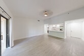 Located at 6415 21st Ave W. in Bradenton, Florida, this well-appointed single-floor residence offers a clean, modern aesthetic throughout. Light wood-look flooring spans the entire living space, complemented by crisp white walls and white baseboards that create a bright, airy atmosphere.

The entry hallway leads into an open-concept combined dining and living area, which is bathed in natural light from a sliding glass door with draping curtains that opens to a spacious enclosed Florida room. The Florida room is a standout feature, wrapped in floor-to-ceiling windows framed in dark trim, offering lush views of surrounding palm trees and filling the interior with abundant Florida sunshine.

The kitchen is accessible via a peninsula counter and features white shaker-style cabinetry, light stone countertops, a stainless steel refrigerator with ice maker, a dishwasher, a range, and recessed lighting — all finished in a cohesive, contemporary style.

The generously sized primary bedroom includes a ceiling fan, a sliding glass door to the Florida room, and access to two closets. The bathroom offers a wide vanity with stone countertops, white cabinetry with gold hardware, a large mirror, and stylish globe lighting. In-unit laundry adds everyday convenience. Ceiling fans are found throughout, keeping the space comfortable year-round.
