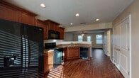 This two-story home offers a thoughtfully designed layout that balances functionality and comfort throughout its two levels. The main floor showcases an open-concept design where the kitchen flows seamlessly into the living area. The kitchen is well-equipped with rich cherry-toned cabinetry, granite-look countertops, and a full suite of black Whirlpool appliances, including a side-by-side refrigerator, electric range, over-the-range microwave, and dishwasher. A double sink and ample cabinet storage complete the space. The adjoining living area features dark hardwood-style flooring, a ceiling fan with light fixture, and multiple windows that invite natural light. A dedicated entry door adds convenient access from this main living space. A staircase connects the two floors, leading to the upper level where carpeted bedrooms provide a comfortable retreat. The primary bedroom benefits from vaulted ceilings and a ceiling fan, enhancing the sense of openness. Bathrooms on both levels feature clean white tub-shower combinations with chrome fixtures and hardwood-style flooring. Neutral warm-toned walls and textured ceilings are consistent throughout, giving the home a cohesive and inviting character.