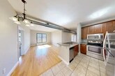 Located at 721 N Clinton St in Syracuse, NY, this thoughtfully designed 3-bedroom, 2-bathroom residence offers a well-appointed single-floor layout with a blend of modern finishes and industrial character. The open-concept living and kitchen area is a standout feature, showcasing warm hardwood flooring, exposed ventilation ductwork that adds an urban loft aesthetic, and a peninsula kitchen with granite countertops, warm wood cabinetry, stainless steel appliances including a refrigerator and dishwasher, and tile flooring. The living area is bathed in natural light from large sliding and picture windows, with a seamless flow to the private balcony offering open views of the surrounding Syracuse skyline and historic brick architecture. The three bedrooms are carpeted for comfort, each with ceiling fans and windows that invite natural light. The generously sized primary bedroom provides ample space for rest and relaxation. Five closets throughout the unit ensure abundant storage. Three hallways connect the rooms efficiently across the single floor. The balcony is a particular highlight, featuring a metal railing and expansive open-air views of the city neighborhood, perfect for enjoying the outdoors.