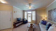 This single-floor 1-bedroom, 1-bathroom residence offers a thoughtfully designed layout that maximizes comfort and functionality. The living room serves as the heart of the home, featuring crown molding, warm neutral-toned walls, and plush carpeting. A ceiling fan overhead provides year-round comfort, while a French door flanked by large windows with elegant drapery fills the space with natural light and provides outdoor access. The open feel is enhanced by a smooth transition from tile at the entry to carpet throughout the main living areas. The galley-style kitchen is equipped with warm wood cabinetry, a full suite of white appliances including a range, over-the-range microwave, and refrigerator, complemented by tile flooring and laminate countertops. A dedicated dining area connects seamlessly to the kitchen and living space. The bedroom is a serene retreat, highlighted by a ceiling fan, a generous window dressed with bright curtains, and soft carpet underfoot. The full bathroom features a tub-shower combination, a rich wood vanity with a large mirror, and tile flooring. Crown molding and consistent neutral tones tie the entire residence together with a cohesive, welcoming aesthetic.