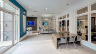 Located at 2211 Parklake Dr NE in Atlanta, GA, this single-story community clubhouse delivers a polished, contemporary amenity experience designed for both socializing and productivity. The open-concept layout is anchored by a bright, airy lounge area featuring a neutral-toned sofa, layered area rugs, and sleek accent furniture arranged beneath an elegant chandelier and shiplap ceiling. Large transom-topped glass-paned doors flood the space with natural light and provide visual connectivity between zones.

A dedicated kitchenette area offers a clean white countertop, undermount sink, under-counter refrigerator, and bar-height seating with modern wire stools — ideal for casual gatherings or catered events. A wall-mounted flat-screen TV adds to the functionality of this entertaining hub.

Adjacent to the main lounge, a game room features a full-size foosball table, a bold teal accent wall with artistic texture, and expansive floor-to-ceiling windows overlooking a landscaped outdoor courtyard with a pergola and lounge seating. A co-working nook with communal table and task seating, along with glass-enclosed private offices visible in the background, supports professional needs. Throughout, light herringbone hardwood flooring, recessed lighting, and curated artwork tie the space together with a cohesive, upscale aesthetic.