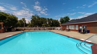 Located at 4211 Fox Rd in Raleigh, NC, this outdoor community amenity space is thoughtfully designed to offer residents a well-rounded recreational experience. At the heart of the space is a generously sized outdoor swimming pool with crystal-clear blue water, bordered by a wide concrete deck and enclosed within a classic white vinyl fence. Lounge chairs are positioned around the pool area, providing ample space for sunbathing and relaxation.

Adjacent to the pool is a brick support building with a pitched shingle roof, offering convenient poolside access. A standout architectural feature of the space is the wood pergola structure, supported by brick columns and surrounded by ornamental grasses and landscaped beds with mulched borders, creating a shaded gathering area ideal for socializing.

The outdoor area also includes a stainless steel grilling station, making it well-suited for outdoor entertaining. Lush mature trees frame the perimeter of the space, offering natural shade and a sense of seclusion. The overall ambiance is clean, welcoming, and community-focused, reflecting a well-maintained residential environment that encourages outdoor living throughout the warmer months.