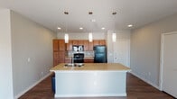 Located at 3001 S New Rd in Waco, Texas, this single-story unit offers a well-designed, open-concept layout that seamlessly connects the kitchen and living areas. The kitchen is a standout feature, showcasing warm honey-toned cabinetry, a mosaic tile backsplash, granite-style countertops, and a large center island with a built-in sink — all illuminated by three stylish pendant lights overhead. Black appliances, including a refrigerator, range, and over-the-range microwave, complete the functional cooking space. The open living area extends naturally from the kitchen, featuring durable hardwood-style flooring, a ceiling fan, and a sliding glass door that invites natural light. The bedrooms are carpeted for comfort, each equipped with a ceiling fan and windows fitted with blinds. Two full bathrooms mirror each other in finish, featuring granite-style vanity countertops, warm wood cabinetry, hardwood-style flooring, and tub-shower combinations. Throughout the unit, neutral gray walls and consistent finishes create a cohesive and clean aesthetic. The thoughtful floor plan, visible in the dollhouse view, provides a practical and comfortable living environment.