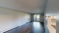 This efficiently designed one-bedroom, one-bathroom unit is laid out across a single floor, offering a functional arrangement of living spaces connected by a central hallway. The living room is a notable highlight, featuring dark hardwood-style flooring, neutral light gray walls, and a wall-mounted air conditioning unit. A sliding glass door fills the room with natural light and provides outdoor access, while dual baseboard heaters along the main wall ensure consistent warmth. The kitchen has been updated with white shaker-style cabinetry, granite-look countertops, stainless steel appliances including a range, microwave, and dishwasher, and a stainless steel sink. A pass-through opening connects the kitchen to the adjoining area, enhancing the sense of openness. The bedroom is carpeted for comfort and includes a built-in closet with double panel doors, offering practical storage. Neutral walls and baseboard heating carry through into the bedroom as well. The bathroom is clean and straightforward, featuring a full tub and shower combination with a curtain rod, a toilet, and wood-look flooring that ties the space together. The overall ambiance is clean, minimal, and move-in ready.