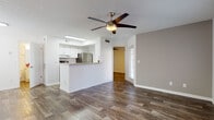 This single-story residence is designed with a clean, modern aesthetic and consistent wood-look flooring that flows throughout every room, creating a cohesive and visually warm interior. The open-concept living area is generously proportioned, with white walls, textured ceilings, and ceiling fans that enhance airflow and comfort. Natural light enters through windows dressed with horizontal blinds, including a distinctive arched window near the entryway that adds architectural character to the foyer.

The kitchen is positioned centrally and defined by a raised breakfast bar peninsula that opens toward the living space. White shaker-style cabinetry lines the walls alongside stainless steel appliances, including a refrigerator and range, with a skylight above providing additional illumination. Granite-style countertops complement the cabinetry throughout.

The bedroom features a sliding closet with panel doors and its own ceiling fan, offering a practical and comfortable retreat. The bathroom presents a long vanity with granite-style countertops, white cabinetry with brushed nickel hardware, a large mirror, and a separate water closet leading to a bathtub with a shower surround. The overall ambiance is bright, neutral, and move-in ready.