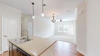 Located at 3815 Maypop Cir in Myrtle Beach, SC, this well-appointed two-bedroom, two-bathroom single-story home offers a thoughtfully designed layout with a clean, neutral aesthetic throughout. The interior opens through a hallway into a kitchen and living area that flow seamlessly together. The kitchen is outfitted with rich dark cabinetry, light stone countertops, a double-basin sink, and black appliances including a refrigerator, range, microwave, and dishwasher. A peninsula with pendant lighting anchors the kitchen and faces the open living room, which features crown molding, a ceiling fan with chandelier-style lighting, and a window that brings in natural light. Hardwood-style flooring runs through the kitchen and main areas, while plush carpet covers both bedrooms. The primary bedroom features crown molding, dual windows with outdoor views, and a ceiling fan. The second bedroom also includes a ceiling fan and a window with natural light. Both bathrooms are finished with granite-top vanities and hardwood-style flooring, with one featuring a full tub-shower combo. A dedicated laundry room houses a full-size washer and dryer with built-in shelving above. Two closets and a hallway complete the functional floor plan of this comfortable Myrtle Beach home.