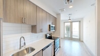 Located at 651 E 6th St in Tempe, Arizona, this efficiently designed one-bedroom, one-bathroom unit offers a thoughtfully laid-out floor plan that maximizes every square foot. Light wood-tone flooring runs throughout, creating a cohesive and airy feel across the entire space.

The galley-style kitchen is a standout feature, outfitted with stainless steel appliances — including an electric range, built-in microwave, and dishwasher — complemented by quartz countertops, a single-basin undermount sink, and warm wood-grain cabinetry that extends to the ceiling for ample storage. A white subway tile backsplash adds a clean, contemporary touch.

The kitchen opens directly into the living area, which benefits from natural light pouring in through large glass doors that lead to a private balcony. A ceiling fan overhead enhances comfort and airflow in this combined living space.

The bedroom is a calm, neutral retreat with light walls, light wood flooring, a ceiling fan, and two windows fitted with blinds that frame views of the surrounding Tempe streetscape.

The bathroom is well-appointed with a wood-grain vanity, quartz countertop, a large framed mirror with modern Edison-style lighting, and a glass-enclosed walk-in shower. The overall design aesthetic is clean, modern, and functional throughout.